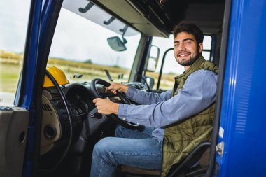 Kamyon kabininde oturan genç profesyonel kamyon şoförü, yoldaki aracı kullanmaya ve çalıştırmaya hazır..