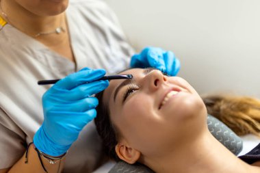 Genç bayan müşteri, temiz ve modern bir güzellik salonunda profesyonel kaş kaplaması (cerrahi olmayan kaş gerdirme olarak da bilinir) yaptırıyor..