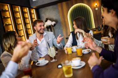 Bir grup şık arkadaş bir restoranda sohbet ediyor ve gülüyor kahve ve meyve suyu yudumluyor, zarif atmosferin ve hareketli sosyal anların tadını çıkarıyor..