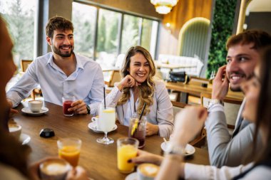Bir grup şık arkadaş bir restoranda sohbet ediyor ve gülüyor kahve ve meyve suyu yudumluyor, zarif atmosferin ve hareketli sosyal anların tadını çıkarıyor..