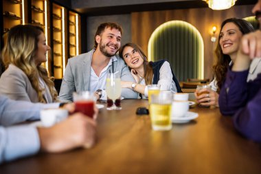 Tarz sahibi arkadaşlar restoranda içki içerken mutlu bir çift kucaklaşır. Zarif kıyafetler, kahve ve meyve suyu, kahkahalar ve çekilen neşeli sosyal anlar..