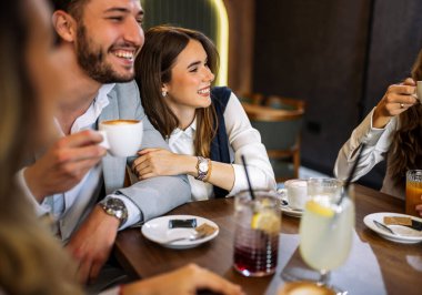 Tarz sahibi arkadaşlar restoranda içki içerken mutlu bir çift kucaklaşır. Zarif kıyafetler, kahve ve meyve suyu, kahkahalar ve çekilen neşeli sosyal anlar..