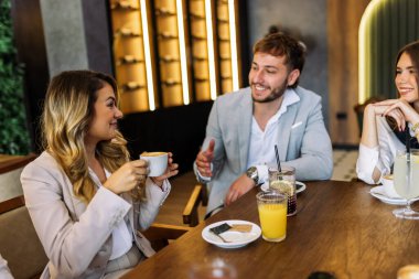 Bir kafede arkadaşlarıyla sohbet ederken kahvenin keyfini çıkaran gülümseyen bir kadın. Sıcak ışık, rahat atmosfer, onun neşeli anına odaklan ve rahatla..