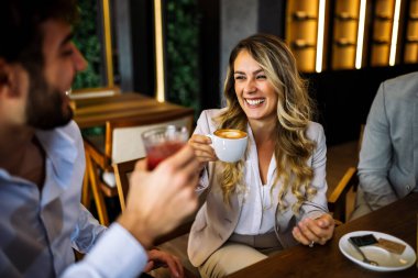 Bir kafede arkadaşlarıyla sohbet ederken kahvenin keyfini çıkaran gülümseyen bir kadın. Sıcak ışık, rahat atmosfer, onun neşeli anına odaklan ve rahatla..