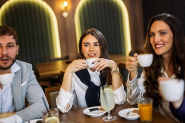 Bir grup şık arkadaş bir restoranda sohbet ediyor ve gülüyor kahve ve meyve suyu yudumluyor, zarif atmosferin ve hareketli sosyal anların tadını çıkarıyor..