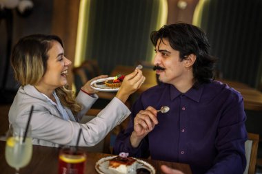 Bir kız arkadaş restoranda erkek arkadaşına kek yedirir. Keyifli, neşeli ve romantik bir an. Sıcak ve şık bir yemek atmosferinde yakalanmış..