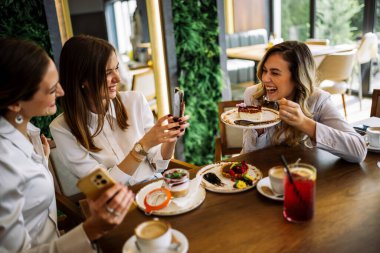 Üç kadın bir restoranda oturup sosyal medya için fotoğraf çekiyor. Keyifli bir gezinti, kahkaha, arkadaşlık ve keyifli anlar şık bir ortamda yakalanır..