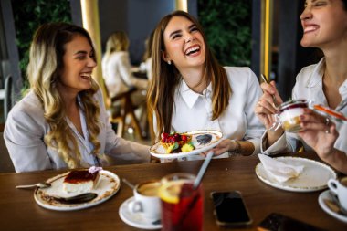 Üç kadın alışveriş yaptıktan sonra bir restoranda oturup pasta tadıyor. Eğlence, arkadaşlık, kahkaha ve şık bir atmosferde yakalanmış samimi sosyal anlar..