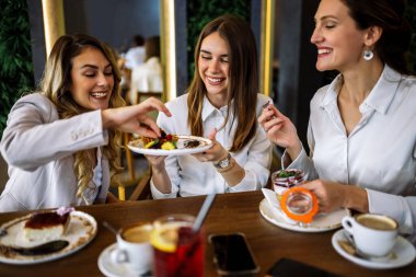 Üç kadın alışveriş yaptıktan sonra bir restoranda oturup pasta tadıyor. Eğlence, arkadaşlık, kahkaha ve şık bir atmosferde yakalanmış samimi sosyal anlar..