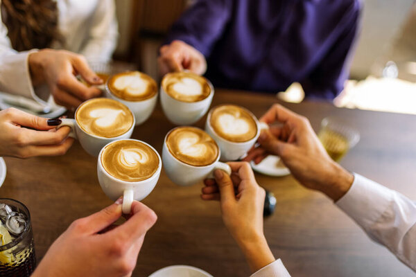 Close-up of friends clinking coffee cups in a cozy cafe.