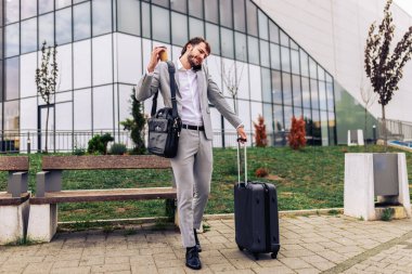 Dışarıda telefonla konuşan, bavul ve kahve fincanı taşıyan meşgul bir işadamı. Kentsel bir ortamda seyahat ederken ya da seyahat ederken modern profesyonel çoklu görev.