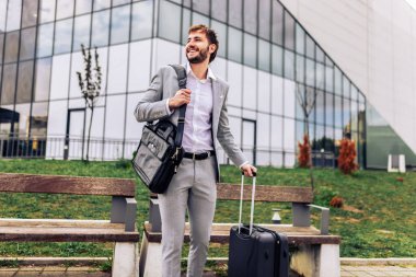 Genç iş adamı iş gezisinde, bavullarını taşıyor ve işleriyle meşgul. Şehirde modern profesyonel seyahat, hareket halindeyken işleri yönetmek..