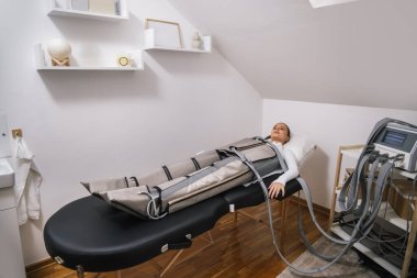 Genç bir kadın, bir sağlık merkezinde basınç terapisi makinesinde yatıyor. Tedavi sırasında dinleniyor..