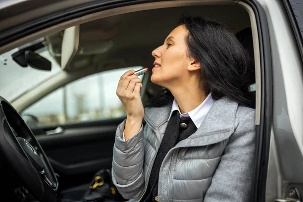 Orta yaşlı bir kadın arabasının camlarını bezle temizliyor.