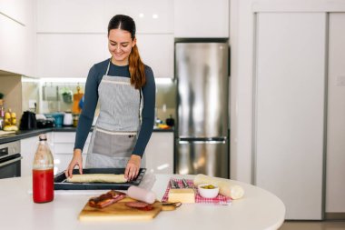 Evde pizza hamurunu pişirme tepsisine döken genç bir kadın ev yapımı pizza yapmaya hazırlanıyor..