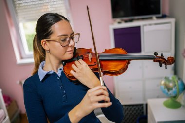 Genç bir keman öğretmeni evde yalnız çalışır, sakin bir melodi çalarken tekniğine odaklanır.