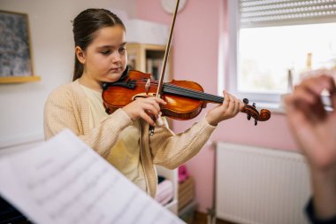 Genç kız evde keman çalışıyor, duruşuna odaklanıyor ve basit bir melodiyi öğrenirken eğiliyor..