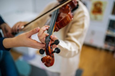 Genç bir keman öğretmeni, bir ev dersi sırasında küçük bir kıza selam verme tekniği ve duruşunda rehberlik eder..
