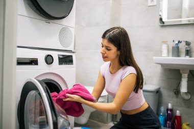 Genç bir kadın banyodaki çamaşır makinesinden yeni yıkanmış havluları alıyor ve onları kokluyor. Temiz ve hoş kokularının tadını çıkarıyor..