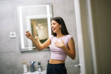 Banyoda genç bir kadın hamilelik testi yapıyor ve mutluluk ve heyecan dolu bir tepki gösteriyor..