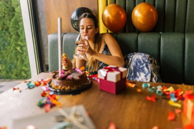 Yorgun bir kız, etrafı konfeti, pasta, hediye ve partilerle çevrili dağınık bir kanepede şarap içer.