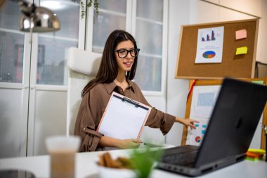 Çevrimiçi bir toplantıda meslektaşlarına grafik ve slayt sunan genç profesyonel bir kadın modern bir ofiste takım çalışması ve üretkenlik gösteriyor..