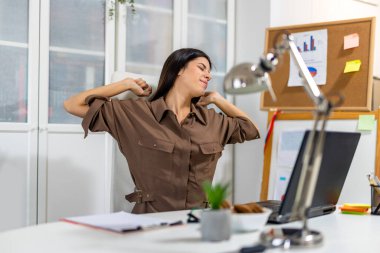 Modern bir ofiste masasında uzanan genç profesyonel bir kadın yorgunluğu atmak ve iş sırasında sağlığını korumak için mola veriyor..