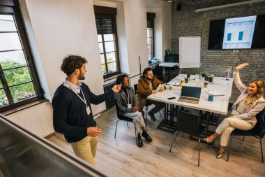 Meslektaşlar konferans masasında katılımlarını, takım çalışmalarını ve işbirliği göstererek dikkatle dinlerken, genç iş adamları bir toplantı sırasında konuşma yapmak için el kaldırıyorlar..