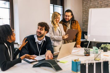 Aralarında siyahi bir kadının da bulunduğu çeşitli ırklardan oluşan genç bir iş ekibi bir dizüstü bilgisayarın etrafındaki konferans odasında oturmuş fikir alışverişinde bulunuyor ve bir proje üzerinde işbirliği yapıyor..