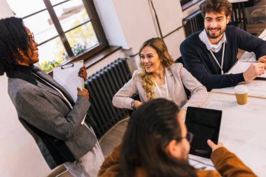 Bir konferans salonunda toplanan, strateji ve fikirleri, çeşitliliği, takım çalışmasını ve modern kurumsal işbirliğini vurgulayan bir grup farklı ırktan genç iş adamı..