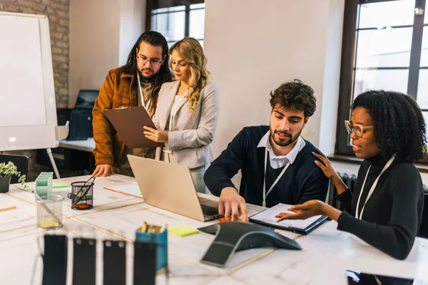 Siyahi bir kadın da dahil olmak üzere farklı ırktan genç iş adamları konferans odasında dizüstü bilgisayarda oturmuş, fikirleri tartışıyor ve işbirliği yapıyor, takım çalışması ve çeşitliliği vurguluyor..
