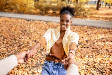 Neşeli Afrikalı Amerikalı çift, sonbahar parkında el ele tutuşup birlikte dönüyor, neşe dolu aşk, kahkaha ve ılık sonbahar enerjisini paylaşıyorlar..