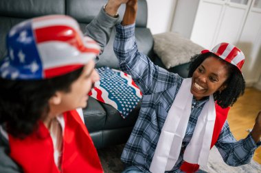 Latin adam ve Afrikalı Amerikalı kız arkadaşı Amerika 'da oy kullanmalarını kutluyor, Amerikan bayrağı takıyor ve seçimleri izlerken mutluluk ve yurttaşlık gururlarını gösteriyorlar..