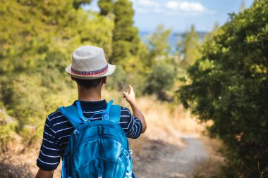Genç bir çocuk yazın sırt çantasıyla yürüyüşe çıkıyor. Açık hava macerası, aktif yaşam tarzı ve doğa keşfi, seyahat ve yaz tatili kavramları için mükemmel..