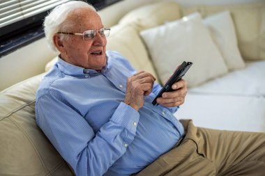 Evde otururken cep telefonu kullanan yaşlı bir adam.