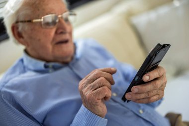 Evde otururken cep telefonu kullanan yaşlı bir adam.