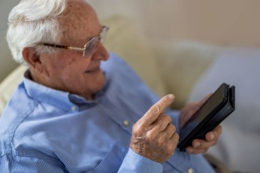 Evde otururken cep telefonu kullanan yaşlı bir adam.