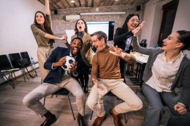 İş yerinde futbol maçı izleyen bir grup iş arkadaşı, bir kişi futbol topunu tutarken birlikte tezahürat yapıyorlar, takım çalışması, heyecan ve pozitif ofis kültürü gösteriyorlar..