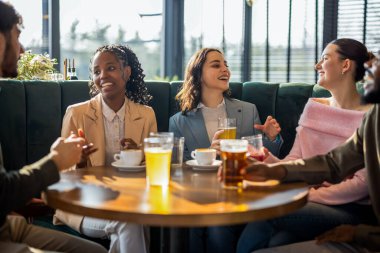 Bir restoranda bira içip eğlenen mutlu bir arkadaş grubu. Sıcak bir sosyal ortamda gülüp rahatlıyorlar..