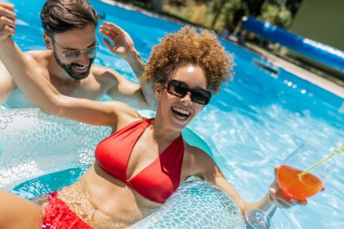 Yüzme havuzunda bir adamla kokteyl içen genç bir kadın.