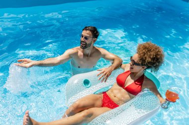 Yüzme havuzunda bir adamla kokteyl içen genç bir kadın.