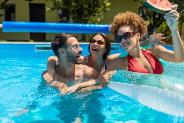 Bir grup arkadaş yüzme havuzunun keyfini çıkarıyorlar, gülüyorlar, su sıçratıyorlar ve eğleniyorlar, yaz için mükemmel, boş zaman, tatil ve arkadaşlık kavramları..