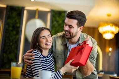 Lokantada oturan bir adam, elinde hediye olan bir kadını şaşırtıyor.