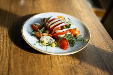 Dilimlenmiş domatesli taze Caprese salatası, mozzarella peyniri ve tabakta fesleğen yaprağı..
