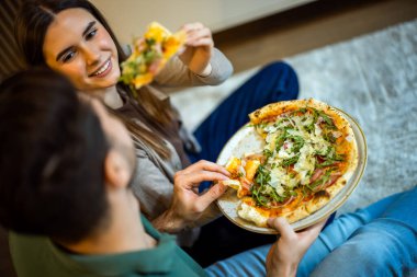 Mutlu çift yerde otururken pizzayı paylaşıyor.