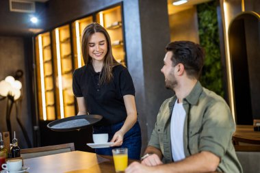 Genç garson bir kafede erkek bir müşteriye kahve ve meyve suyu servisi yapıyor..