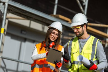 Genç erkek ve kadın mühendisler inşaat alanında dijital tablet kullanarak bir proje üzerinde çalışıyorlar..