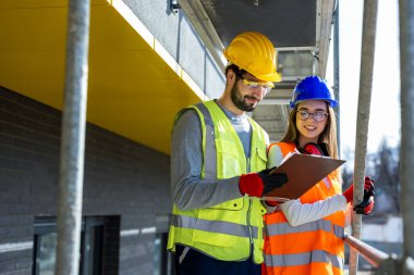 Erkek ve kadın mühendisler güvenlik ekipmanlarıyla inşaat alanında profesyonel bir tartışma yapıyorlar..