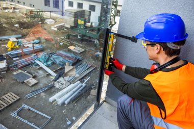 Güvenlik donanımlı iki profesyonel müteahhit modern cam balkon korkuluklarını ölçüyorlar. Çağdaş bir binada kurulum sürecinde kusursuz yatay hizalama ve hassasiyet sağlamak için bir ruh seviyesi aracı kullanıyorlar.