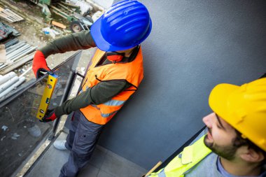Güvenlik donanımlı iki profesyonel müteahhit modern cam balkon korkuluklarını ölçüyorlar. Çağdaş bir binada kurulum sürecinde kusursuz yatay hizalama ve hassasiyet sağlamak için bir ruh seviyesi aracı kullanıyorlar.
